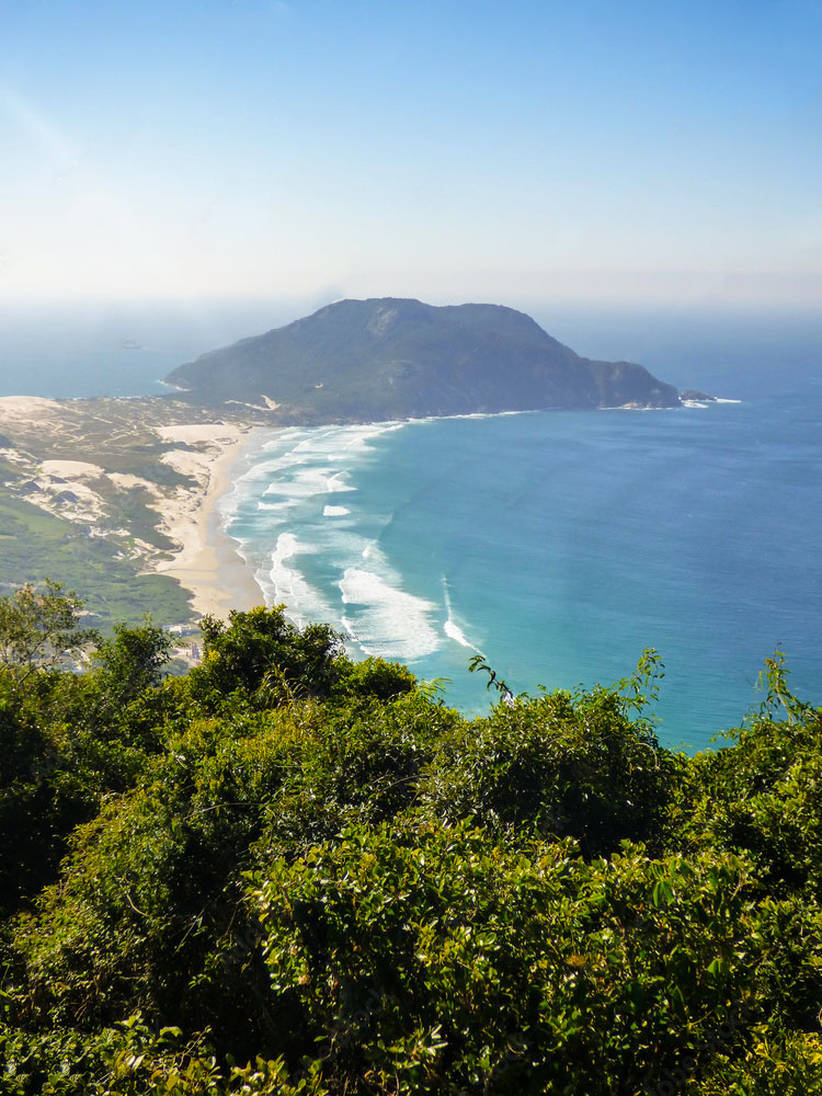 Vista do alto do Morro das Aranhas sobre a praia do Santinho, em Florianópolis, com o campo de dunas à esquerda e a ponta rochosa ao fundo