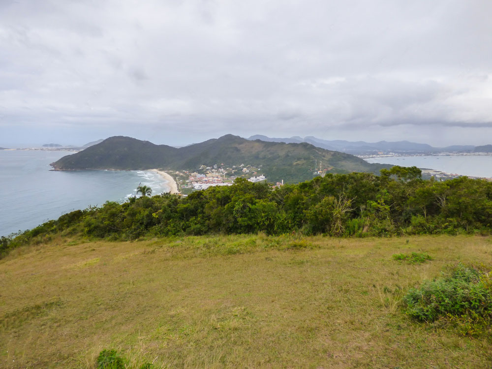 Vista do campo no alto do Morro do Rapa, em Florianópolis, sobre a praia e a vila abaixo, em dia nublado
