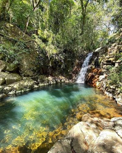 Queda d'água caindo num poço de água verde e transparente, cercado de rocha e mata, no Poção do Córrego Grande em Florianópolis